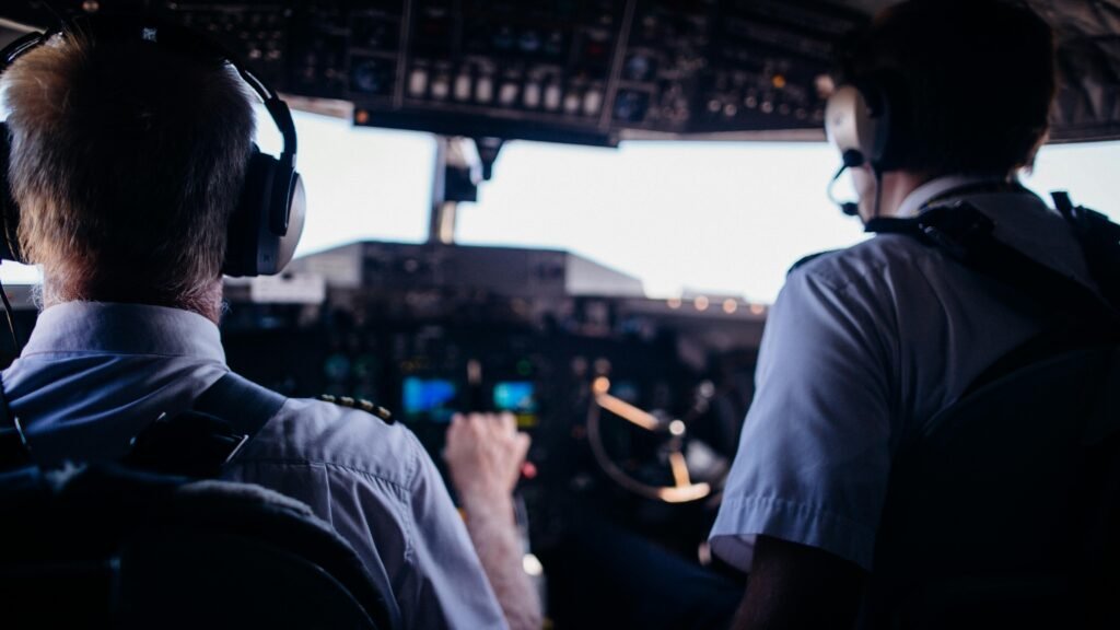 Back view of anonymous male pilots in uniform and headset navigating modern airplane while taking off